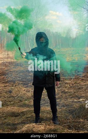 Ein Teenager in einer schwarzen Jacke und einer Maske hält eine grüne Rauchbombe Stockfoto