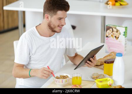 Junger Mann trinkt Kaffee und liest die Nachrichten auf Tablet Stockfoto