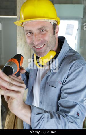 Lächelnder Handwerker mit Elektrobohrer in geräumiger Werkstatt Stockfoto