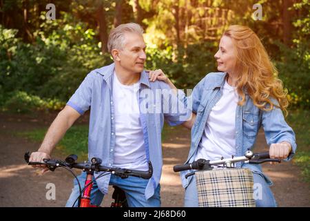Fröhliches aktives Seniorenpaar mit Fahrrad, das gemeinsam durch den Park läuft. Perfekte Aktivitäten für Senioren im Ruhestand Lebensstil tragen Casual tragen tragen lächelnd Stockfoto