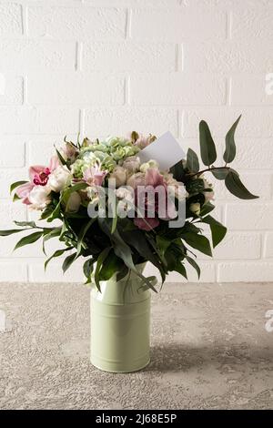 Ein Strauß frisch geschnittener Gartenblumen in einer modernen Vase steht auf einem Tisch mit einer Textkarte. Das Ende des Geschenks, die Aufmerksamkeit der Liebsten Stockfoto