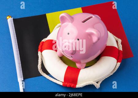 Sparschwein, Rettungsring und Flagge auf blauem Hintergrund, das Konzept der Rettung der belgischen Wirtschaft Stockfoto