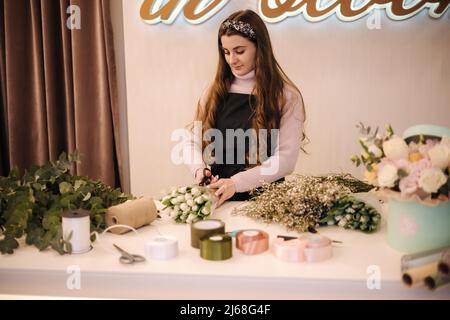 Blumenlieferungsladen. Florist, der Ordnung schafft, Frühlingsstrauß macht. Weiblich machen Bouquet mit Tulpen Stockfoto