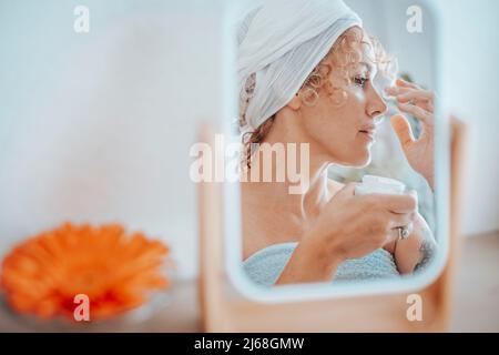 Schöne junge Erwachsene Frau, die sich zu Hause um ihre Haut kümmert. Frau spiegelt sich in einem Spiegel in Schönheit Freizeit Aktivität. Hautpflege und Cremes für die Hautalterung p Stockfoto