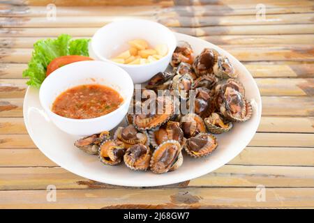 Parboiled Herzmuscheln oder blutige Herzmuscheln mit würziger Thai-Dip-Sauce und Knoblauch auf Bambus-Tischhintergrund. Stockfoto