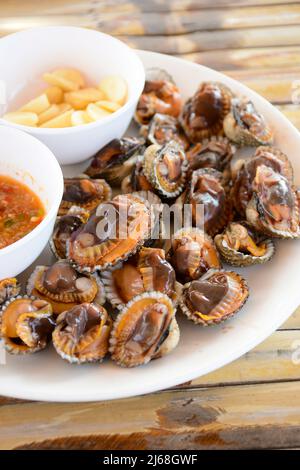 Parboiled Herzmuscheln oder blutige Herzmuscheln mit würziger Thai-Dip-Sauce und Knoblauch auf Bambus-Tischhintergrund. Stockfoto