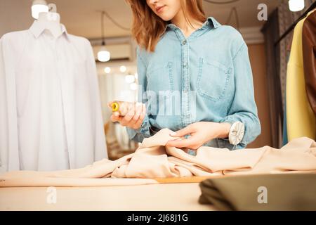 Näherin im Atelier arbeitet mit beigem Stoff, Werkstatt. Handarbeit, Kleinunternehmen. Stockfoto