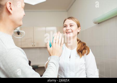 Schöne weibliche Zahnärztin im Büro in der Klinik, zufriedene glückliche Klientin schüttelt die Hände, ausgezeichneter professioneller Service. Klatschen Stockfoto