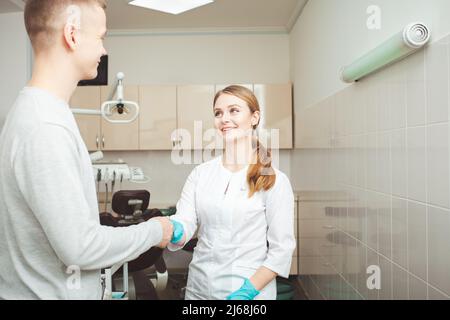 Schöne weibliche Zahnärztin im Büro in der Klinik, zufriedene glückliche Klientin schüttelt die Hände, ausgezeichneter professioneller Service. Stockfoto