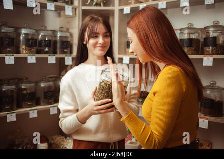 Frau wählt Tee im Laden, natürliche chinesische Kräuter in Gläsern auf Wind. Privatunternehmen, Unternehmer, Verkauf von Waren. Junger Verkäufer Stockfoto