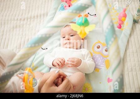 Kind liegt auf dem Bett, hängende Spielzeug, Babymatte, neugeborenes Mädchen. Entwicklung, beobachten Spielzeug zufrieden Stockfoto