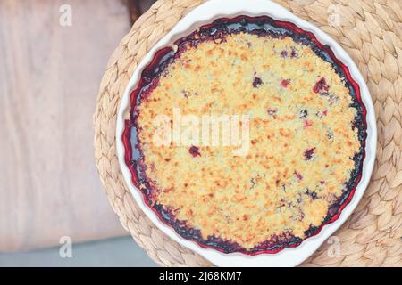 Beerenkrümelkuchen in Backform auf natürlichem Tischset auf einem Tisch. Sommerdessert. Schusterpastete mit frischen, im Garten angebauten Beeren Stockfoto