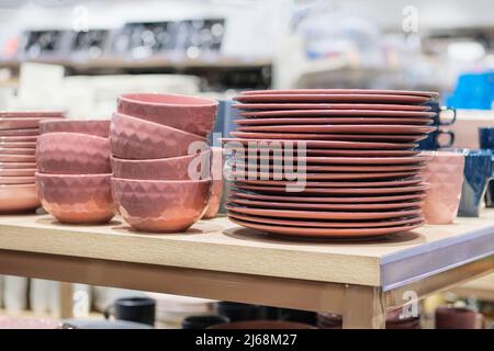 Gerichte werden im Laden verkauft. Reihen von verschiedenen rosa Schalen und Teller für zu Hause auf Regalen in einem Supermarkt. Stockfoto