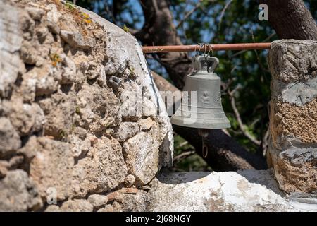 Alte Metallglocke in einem Bauernhof auf einer Steinmauer. Stockfoto