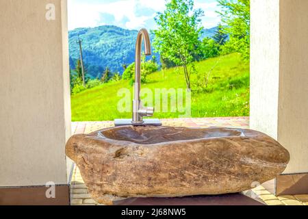 Steinwaschbecken im Frühling Sonnenlichthof. Modernes Waschbecken im Sommerhinterhof bei sonnigem Licht. Ländliche Landschaft mit natürlichen Felsen Waschtisch von Berg BA Stockfoto