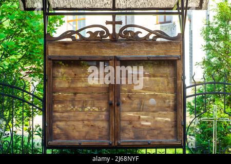 Kirche hölzerne leere Tafel auf der Straße. gemeinderat vor der Tafel hinter Glas. Alter Holzstand mit Kreuz für Anzeigen oder Informationen in der Stadt Stockfoto