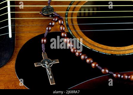 Kruzifix aus Messing und Rosenkranz aus Holz auf einer Mahagoni-Akustikgitarre Stockfoto