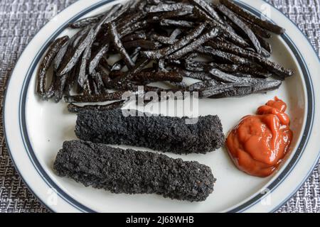 Ein Teller mit stark verbrannten, schwarzen, Fischfingern und Pommes Frites. Stockfoto