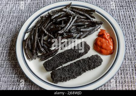 Ein Teller mit stark verbrannten, schwarzen, Fischfingern und Pommes Frites. Stockfoto