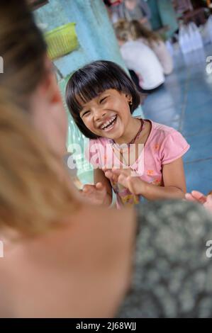 Eine freiwillige Studentin, die im Kinderhaus in Sangkhlaburi ein Spiel mit einem jungen Mädchen spielt, das mit der Hand klatscht. Kanchanaburi. Thailand Stockfoto