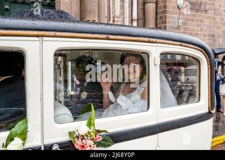 Eine peruanische Braut winkt den Gästen von ihrem Hochzeitsauto zu, nachdem sie in der Kathedrale, Cusco, Provinz Cusco, Peru geheiratet hat. Stockfoto