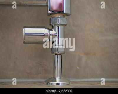 Bodenmontierter Chrom-Heizkörper im Badezimmer mit Nahaufnahme des Thermostatventils Stockfoto
