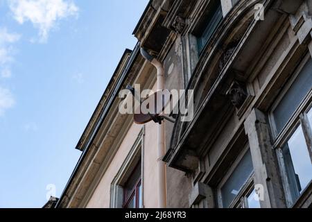 Rostige Satellitenschüssel an einer alten verwitterten Fassade eines Gebäudes. Fernsehtechnologie an der Wand eines Hauses. Vintage-Architektur vor blauem Himmel Stockfoto