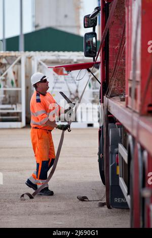 LKW-Fahrer mit Ratschenriemen auf einem Tieflader-LKW, der Offshore-Container transportiert Stockfoto