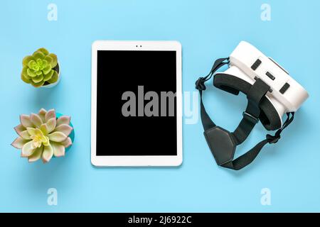 Weißes Tablet mit schwarzem Display, VR-Brille für Virtual-Reality-Spiele auf blauem Hintergrund Draufsicht Flat Lay Mock Up Technology Concept Platz zum Kopieren. Stockfoto