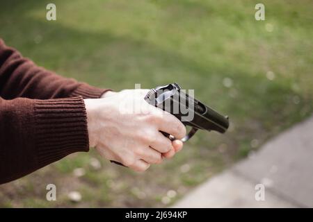 Ein junger Mann erhebt eine Waffe gegen ein grünes Gras. Schusswaffe im Freien. Sport, Hobbys kopieren Platz Stockfoto