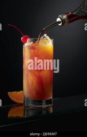 Tequila Sunrise alkoholischer Cocktail in einem hohen Glas. Grenadine wird in ein Glas gegossen. Stockfoto