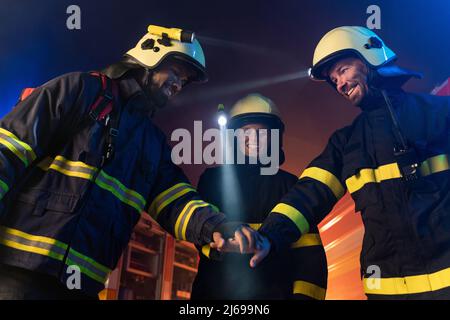 Glückliche Feuerwehrleute Männer und Frau nach erfolgreicher Aktion mit Feuerwehrauto im Hintergrund in der Nacht Stockfoto