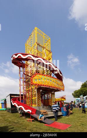 Helter Skelter Ride; ein Kind, das an einem sonnigen Frühlingstag auf der East Anglian Game & Country Fair in Suffolk, Großbritannien, eine Helter Skelter-Fahrt hinunterkommt Stockfoto