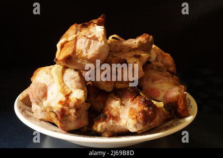 Stücke gebratenes Schweinefleisch auf einem Teller auf dem Tisch. Essen auf schwarzem Hintergrund Stockfoto