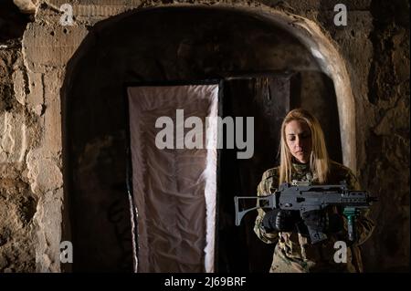 Kaukasische Frau in Armeeuniform, die ein Maschinengewehr hält und in der Nähe eines offenen Sarges steht. Stockfoto
