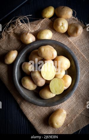 Rohe neue Kartoffeln in einem rustikalen Gericht auf einem dunklen Holztisch. Stockfoto