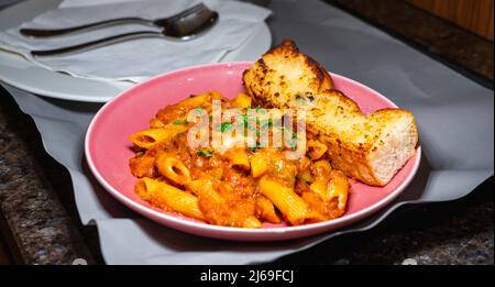 Selektiver Fokus von Penne Arrabiata und Knoblauchbrot auf einem rosa Teller. Stockfoto