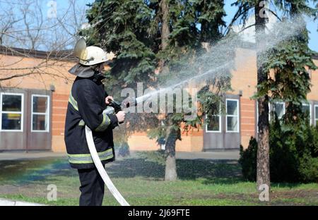 Feuerwehrmann im Schutzkostüm Bewässerung Pflanzengebiet mit Spritze - Rettungsteam Training der Brandbekämpfung. 5. April 2019. Forstwirtschaft des distrikts Sviatoshyn Stockfoto