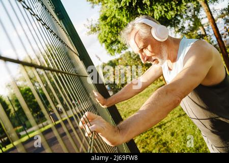 Grauer älterer Mann, der Musik hört und Sport macht, während er draußen trainiert Stockfoto