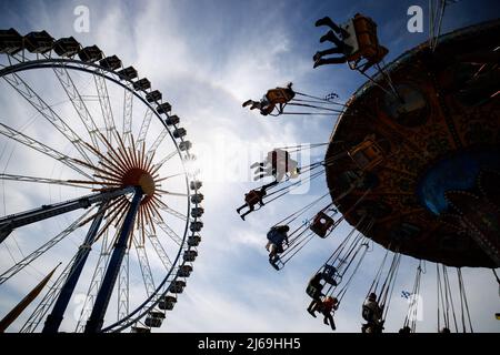 München, Deutschland. 29. April 2022. 29. April 2022, Bayern, München: Besucher des Frühlingsfestes fahren auf der Theresienwiese mit einem Karussell, während im Hintergrund die Sonne hinter einem Riesenrad zu sehen ist. Das Frühlingsfest läuft vom 22,04. Bis 08.05.2022. Foto: Matthias Balk/dpa Quelle: dpa picture Alliance/Alamy Live News Stockfoto