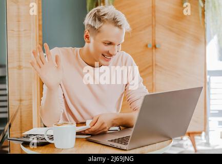 Glücklicher Geschäftsmann, der mit Laptop und Smartphone in der Cafeteria sitzt. Geschäftsmann schreibt auf dem Smartphone, während er in einem Café sitzt, arbeitet und e überprüft Stockfoto