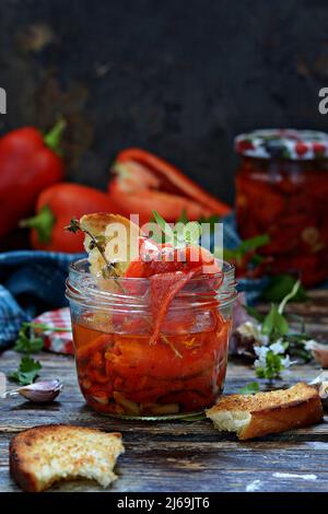 Getrockneter (gebackener) bulgarischer roter Pfeffer, Paprika mit Kräutern Rosmarin, Thymian, Majoran, Knoblauch mit Olivenöl in einem Glas und eine Scheibe Brot. Italienisch A Stockfoto
