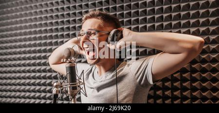 Die Sängerin singt im Studio mit einem Mikrofon. Ein Mann mit Kopfhörern schreibt einen Podcast, ein Hörbuch. Künstler, Aufnahme eines Albums, Arbeit mit dem Label Stockfoto