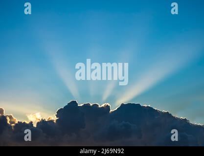 Sonnenstrahlen hinter Wolken am blauen Himmel Stockfoto