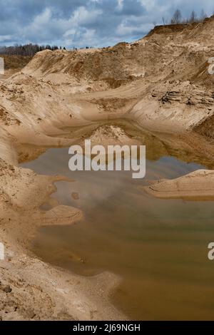 Sanddünen auf allen Seiten und ein künstlicher Teich in der Mitte. Eine kleine Insel aus Sand im Wasser. Spiegelreflexion im klaren Wasser bei sonnigem Wetter. Stockfoto