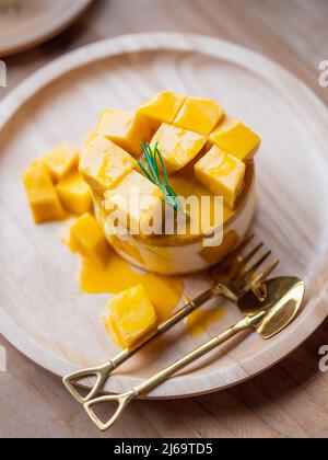 Süßer gelber Mango-Käsekuchen auf runder Holzschale Stockfoto