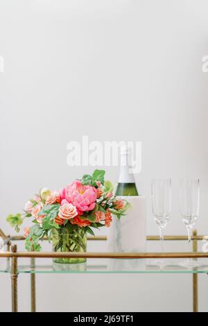 Rosafarbene Blumen auf Barwagen mit Champagner-Flasche und zwei Gläsern Stockfoto