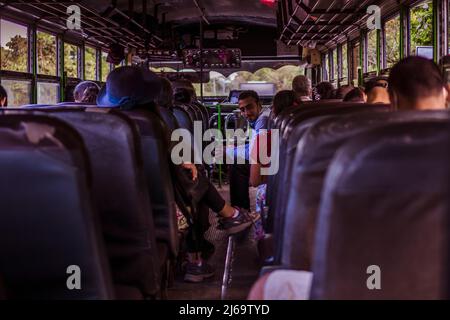 Juayua, El Salvador - 29. Januar 2022: Blick von innen auf die Rückseite eines Busses in El Salvador. Pendler, die auf abgenutzten Sitzen sitzen Stockfoto