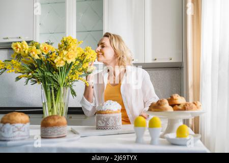 Eine Frau mit ostergebäck und einem Blumenstrauß aus gelben Blumen. Stockfoto