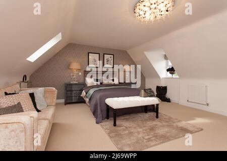 Loft-Umbauschlafzimmer mit Sofa, Bett und Dachfenstern zu beiden Seiten. Stockfoto